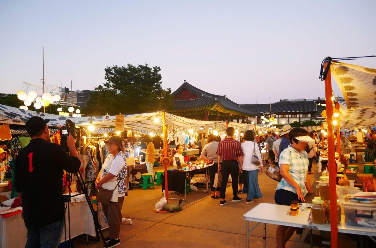 夜市現場，日落後市集燈光明亮，絡繹不絕的遊客在傳統建築前徘徊。